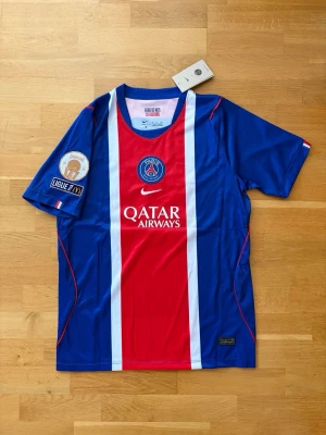 PSG matchtröja O. Dembélé #10 - Säljer en officiell PSG matchtröja från Nike med O. Dembélé och nummer 10 på ryggen. Tröjan är blå med röda och vita detaljer, har Qatar Airways som sponsor och Ligue 1-märke på ärmen. Perfekt för fotbollsfans som vill stötta sitt lag.