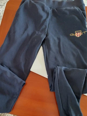 Mörkblå mjukisbyxor från GANT - Snygga mörkblå mjukisbyxor från GANT med broderad logga och emblem på ena benet. Byxorna har resår i midjan och är gjorda i mjukt bomullsmaterial. Perfekta för en avslappnad och chill stil.