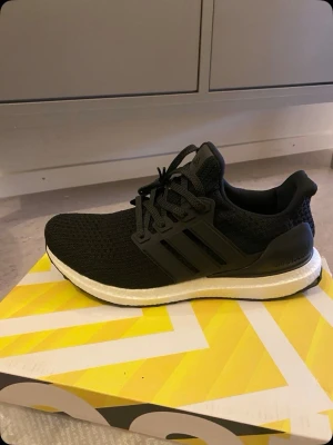 Ultra boost - Svarta Adidas sneakers med stickad ovandel och klassiska tre ränder på sidan. Skorna har en vit, dämpad sula och svarta skosnören. Perfekta för en sportig och stilren look. Ovandelen är i meshmaterial för extra komfort.
