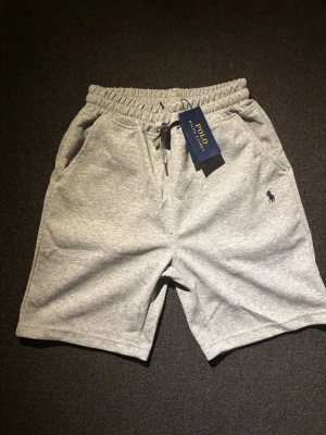 Polo Ralph Lauren shorts - Snygga grå shorts från Polo Ralph Lauren med elastisk midja och snörning. Mjukt material och klassisk logga broderad på ena benet. Perfekta för en avslappnad stil och enkel att matcha med t-shirt eller hoodie.