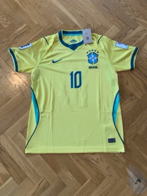 Neymar JR Gul Brasilien fotbollströja Nike - Snygg gul Brasilien fotbollströja från Nike med nummer 10 på bröstet och blå detaljer vid ärmar och sidor. Tröjan har korta ärmar, rund halsringning med blå kant och officiellt Brasilien-emblem på bröstet. Perfekt för match eller träning. 349kr pris kan diskuteras 