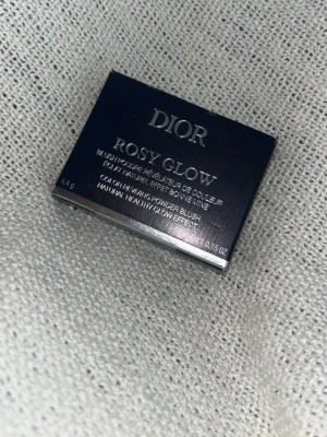 Dior Rosy Glow puderrouge - Dior Rosy Glow är ett puderrouge i en snygg rosabrun nyans. Kommer i en elegant, rektangulär dosa med spegel och tydlig Dior-logga. Rouget har en silkeslen formula som ger en naturlig glow och fräsch finish till kinderna.