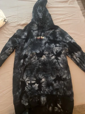 Svart tie-dye hoodie med huva - Säljer en oversized svart och grå tie-dye hoodie med stor huva och magficka. Hoodien har dragsko i huvan och ett litet tryck på bröstet. Perfekt för dig som gillar streetwear och vill sticka ut med en unik look.