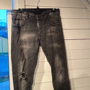 Svarta jeans från DSQUARED2 - Snygga svarta jeans från DSQUARED2 med slitna detaljer och en cool tvättad look. De har en klassisk femficksdesign och knappgylf. Perfekta för en trendig stil. Byxorna är i fint skick men man bedömer själv efter bilderna!                                                                          Hör av er vid minsta lilla!                                                   Kan frakta📦