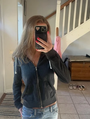 Mörkgrå zip hoodie - Säljer en mörkgrå hoodie med dragkedja och huva. Tröjan har vita snören i huvan, två fickor framtill och ribbade muddar vid ärmslut och nederkant. Bra skick 