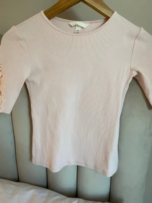 Ljusrosa ribbad topp med spetsärm💓 - Jag säljer en ljusrosa topp/t-shirt med ribbad struktur och korta ärmar dekorerade med spetsdetaljer. Rund halsringning och figurnära passform.💞