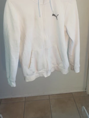 Vit hoodie med dragkedja från Puma - Säljer en vit hoodie från Puma i storlek M passar också S. Hoodien har dragkedja framtill, två stora fickor och en klassisk huva med snören. Puma-loggan sitter broderad på bröstet. Perfekt för en chill och sportig look.