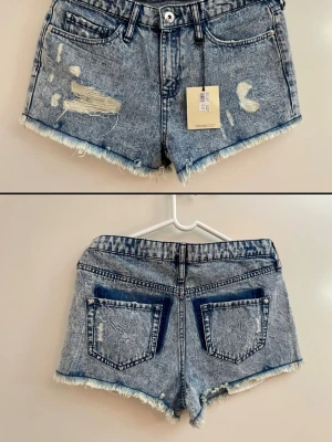 Blå slitna jeansshorts River Island stl M /38 nya  - Snygga blå jeansshorts från River Island med slitna detaljer och fransig kant. Klassisk femficksmodell med knapp och dragkedja framtill. Perfekta för sommaren och ger en avslappnad vibe till din outfit. Stl M / 38 buyikpris ca 450kr 