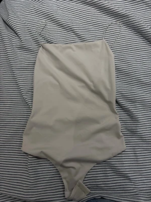 Beige body med tunna axelband H&M - Säljer en stilren beige body från H&M med tunna axelband och enkel design. Materialet är mjukt och stretchigt, vilket gör den bekväm att bära. Perfekt att styla under skjortor eller tröjor för en clean look.