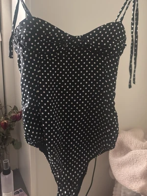 Svart baddräkt med vita prickar Zara - Snygg svart baddräkt från Zara med vita prickar och tunna axelband som knyts. Söt sweetheart-ringning och figurnära passform. Perfekt för strand eller poolhäng. Materialet är stretchigt och bekvämt. Prislapp kvar