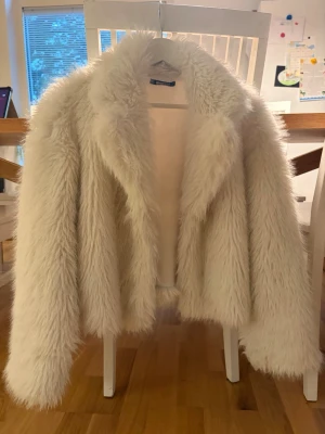 Vit fluffig fuskpälsjacka - Säljer en supermjuk och fluffig vit fuskpälsjacka med bred krage och långa ärmar. Jackan har en oversized look och är perfekt för dig som vill sticka ut med en trendig och cozy stil. Passar till alla som älskar statement-plagg och vill ha något extra i garderoben.