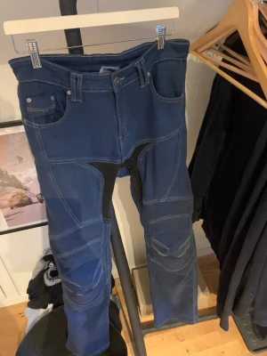 Blå mc jeans, AA skydd - Säljer ett par blå mc jeans med coola förstärkta partier och kontrastsömmar. Jeansen har fem fickor, bälteshällor och detaljer i svart tyg vid grenen och knäna. Snygg passform och perfekt för dig som gillar en lite tuffare stil. Endast använda 2 gånger och är som nya, nypris är 1600 kronor mitt pris 1299