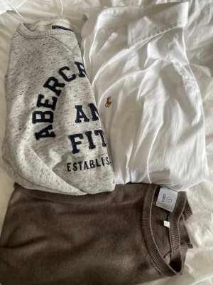 3-pack BULK tröjor - Säljer ett paket med tre tröjor: en grå sweatshirt från Abercrombie & Fitch med tryck, en vit skjorta från Polo Ralph Lauren med broderad logga och en brun stickad tröja. Perfekt för dig om du är intresserad av att resella. Riktigt fynd och bra pris, kolla profil för 2 till paket med andra storlekar, inga frågor, pris ej huggit i pris!!