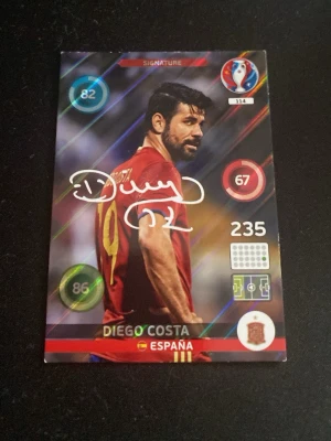 Samlarbild Diego Costa Spanien - Säljer en samlarbild med fotbollsspelaren Diego Costa från Spanien. Kortet har färgstarka detaljer, spelarens namn och landslagets logga. Siffror och symboler syns på framsidan samt en tryckt autograf. Perfekt för dig som gillar fotboll och samlarkort.