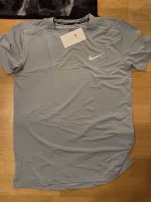 Grått träningsset från Nike - Säljer ett grått & ett svart träningsset från Nike med t-shirt och shorts. T-shirten har rund hals och korta ärmar, medan shortsen har resårmidja och snörning. Båda plaggen har Nike-logga framtill och är tillverkade i ett lätt, syntetiskt material som andas. Fler exemplar finns