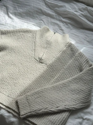 Quarter Zip sweater - Mysig beige stickad tröja med halv dragkedja och hög krage. Tröjan har en grovstickad struktur och långa ärmar. 