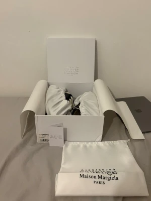 Maison Margiela GATS strl 42 svart/gummi - Maison Margiela sneakers i svart och vitt med klassisk låg silhuett. Skorna har vita snören och detaljer i beige. Kommer i originalkartong med dustbags . Perfekta för dig som gillar stilrena och exklusiva sneakers. Skickas alltid inom 24h