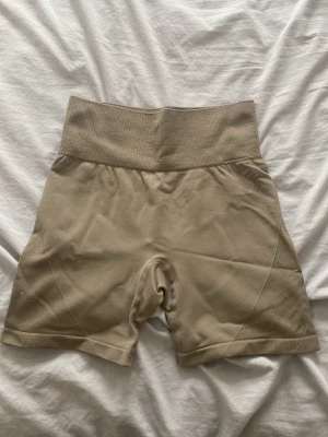Beige högmidjade cykelshorts - Snygga beige cykelshorts med hög midja och ribbade detaljer i midjan. Shortsen har en tight passform och är tillverkade i ett stretchigt material som passar perfekt till träning eller chill. Stilrena och enkla att matcha med olika toppar.