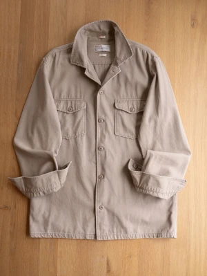 These Glory Days Beige overshirt, size L - Stilren beige overshirt i bomull med två bröstfickor med lock och knapp. Klassisk krage och knäppning framtill. Perfekt lager-på-lager-plagg för en avslappnad look. Långa ärmar med knapp vid ärmslut.