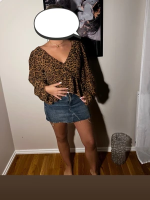Brun leopardmönstrad topp - Snygg brun topp med leopardmönster och långa ärmar. Djup v-ringning både fram och bak ger en trendig look. Tunt, lätt material som faller fint och markerar midjan. Perfekt för dig som vill sticka ut med ett djuriskt mönster.