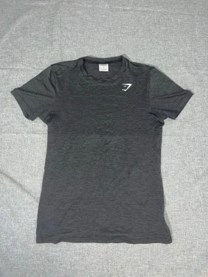 Mörkgrå träningströja Gymshark - Snygg mörkgrå träningströja från Gymshark i funktionsmaterial. T-shirten har korta ärmar. Använd fåtal gånger. Pris går att diskuteras! 😊