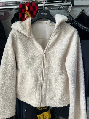 Teddyjacka hm - Mysig vit teddyjacka i storlek XS med dragkedja framtill och två stora fickor. Jackan har en skön huva och är gjord i fluffigt teddy-material som håller dig varm. Perfekt för kyliga dagar när du vill vara både bekväm och snygg.