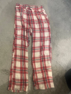 Rutiga pyjamasbyxor i rött och vitt - Mysiga pyjamasbyxor med rött, vitt och grått rutmönster. Byxorna har resår i midjan och dragsko för extra komfort. Tillverkade i mjukt tyg, perfekta för slappa dagar hemma eller en skön natts sömn.