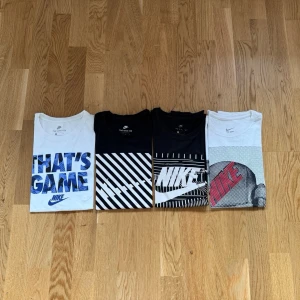 4 st Nike T-shirts - Fyra snygga t-shirts från Nike med olika grafiska tryck. Två vita och två svarta, alla med korta ärmar och coola mönster i blått, vitt och svart. Perfekta för dig som gillar sportig och trendig stil.