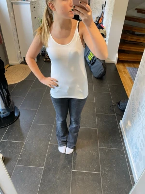 Vit baslinne med smala axelband - Säljer ett enkelt vitt linne med smala axelband och rundad halsringning. Perfekt att ha som basplagg till olika outfits. Linnet är i mjukt material och har en rak passform.