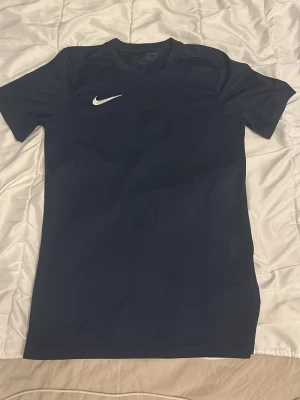 Mörkblå Nike t-shirt - Snygg mörkblå t-shirt från Nike med klassisk vit logga på bröstet. T-shirten har korta ärmar och rund halsringning. Perfekt till vardags eller träning för en sportig look.