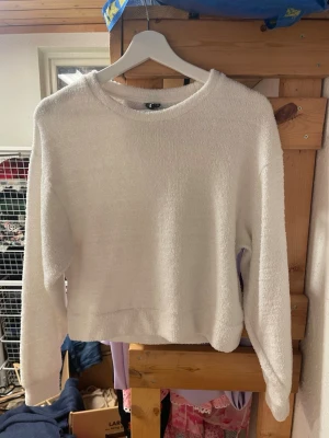 Vit fluffig stickad tröja - Mysig vit stickad tröja med fluffig textur och rund hals. Tröjan har långa ärmar och en avslappnad passform, perfekt för kyliga dagar. Materialet ser ut att vara mjukt och bekvämt, vilket gör den extra skön att bära.