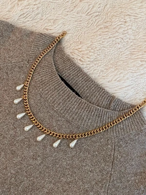 Guldfärgat halsband med pärldroppar - Snyggt halsband i guldfärgad metall med kedja och sju droppformade pärlor som hänger längs framsidan. Perfekt accessoar för att lyfta din outfit med en elegant touch och trendig vibe.