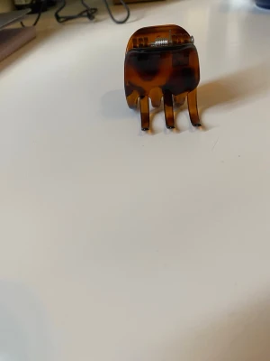 Liten Brun hårklämma i sköldpaddsmönster - Snygg liten hårklämma i klassiskt sköldpaddsmönster med bruna och svarta toner. Tillverkad i plast med metallfjäder och har en rundad form med fyra greppiga klor. Perfekt för att snabbt sätta upp håret på ett stilrent sätt.