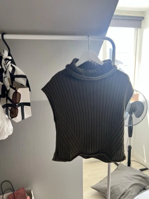 Olivgrön  tröja - Snygg olivgrön ribbstickad tröja med polokrage och ärmlös design. Tröjan har en cool struktur med diagonala och vertikala ränder som ger en modern look. Perfekt att styla över en långärmad topp eller t-shirt.