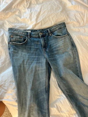 Zara jeans - Säljer ett par klassiska blå jeans med rak passform och lätt slitna detaljer. Jeansen har fem fickor, bälteshällor och knappgylf. Materialet är denim i bomull och färgen är mellanblå med tvättade partier för en avslappnad look.