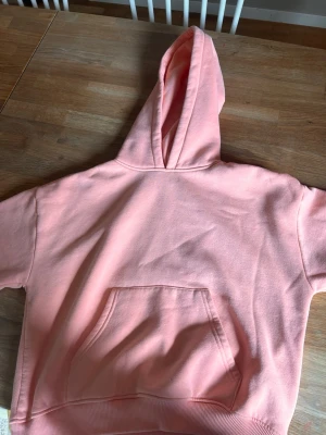 Ljusaprikos hoodie med långa ärmar - Säljer en ljusrosa hoodie med långa ärmar och stor känguruficka framtill. Hoodien har ribbade muddar nedtill och är gjord i mjukt sweatshirtmaterial. Perfekt för en chill och avslappnad stil. (Ljuset är dåligt på alla bilder men jag har en bild från hemsidan)