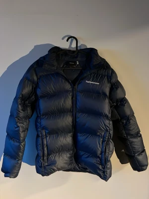 Svart dunjacka Peak Performance - Snygg svart dunjacka från Peak Performance med huva och dragkedja framtill. Jackan har två sidofickor med dragkedja och en puffig, quiltad design som håller dig varm under kalla vinterdagar. Perfekt för dig som vill ha både stil och funktion. Stolek 170 Andvänd en halv vinter så väldigt bra skick på den ny pris 2899kr