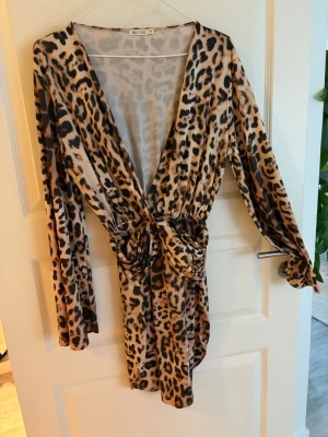 Leopardmönstrad omlottklänning - Snygg kort leopardmönstrad klänning med omlott och knyt i midjan. Djup v-ringning och långa ärmar ger en trendig look. Perfekt för dig som vill sticka ut med ett djuriskt mönster. Materialet känns mjukt och följsamt.