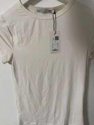 Vit basic t-shirt i bomull - En enkel och stilren vit t-shirt i mjuk bomull. T-shirten har rund halsringning och korta ärmar, perfekt för en clean och avslappnad look. Passar till allt och är ett måste i garderoben. Helt ny med lappen på!  