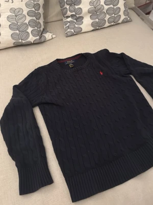Mörkblå kabelstickad Polo Ralph Lauren sweater - Mörkblå kabelstickad tröja från Polo Ralph Lauren. Den är inte så använd iaf inte om man bara kollar på den, bra skick och funkar ja till vardags och på lite finare ställen. Ord pris gick för 1500-2000 kr så jag tycker priset är rimligt med tanke på att den inte har några skador. Den funkar perfekt på en som är från 155-165 cm lång