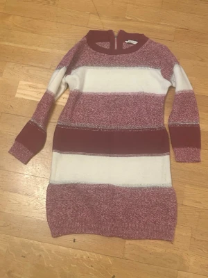 Randig lila och vit stickad klänning - Mysigt med långa ärmar och rund halsringning. Klänningen har ett randigt mönster i olika nyanser av lila och vitt, med inslag av glittrande trådar som ger en festlig touch. Dragkedja baktill i nacken. 💜🤍❄️ Aldrig använt eftersom den var för liten för mig. Mötes I t-centralen eller slussen