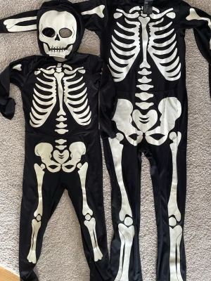 Svarta skelettdräkter med huva - Två svarta helkroppsdräkter med vita skelettmotiv, perfekta för halloween eller maskerad.  Storlek: 110/116 och 134/140. 100:-/st eller 150 för båda