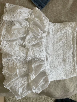 Vit volangkjol från Gina Tricot - Supersöt vit kortkjol från Gina Tricot med broderade spetsdetaljer och volanger. Kjolen har smock i midjan för en bekväm passform och är gjord i bomull. Perfekt för sommarens alla tillfällen! 