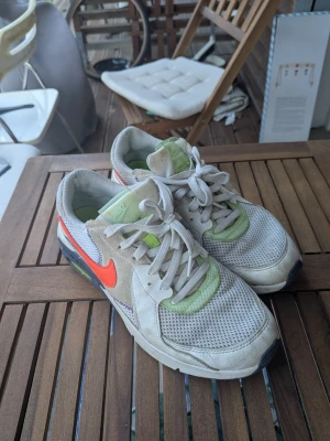 Nike vita sneakers med neon och rött - Nike sneakers i vitt mesh och mocka med neongröna och röda detaljer. Klassisk låg modell med synlig Air-sula och snörning. Swoosh-logga i rött på sidan och gröna detaljer på häl och plös. Lite smutsiga men går nog att göra rent så de blir fina