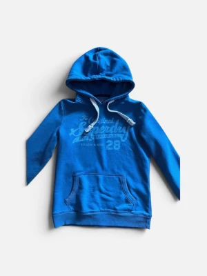 Blå hoodie med tryck och ficka - Snygg blå hoodie med tryck framtill och stor känguruficka. Huvan har vita dragsnören och tröjan är tillverkad i mjukt bomullsmaterial. Perfekt för en avslappnad och cool stil. Långärmad modell med ribbade muddar.
