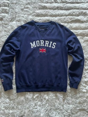 Morris sweatshirt i marinblå - stl L - Morris sweatshirt i marinblå, storlek L. 80% bomull, 20% polyester, rund hals med V-kil, ribbade muddar och nederkant, broderad Morris-text och Union Jack på bröstet.  Använd men i mycket fint skick, inga hål eller fläckar. Personen på bilden är 189cm, väger 78kg.  Rök- och djurfritt hem. Skriv gärna om du vill ha fler bilder eller undrar något!