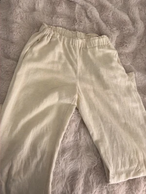 Beiga linnebyxor med resårmidja - Snygga beiga linnebyxor med avslappnad passform och resår i midjan. Byxorna har raka ben och sidfickor, perfekta för en chill och stilren look. Tillverkade i ett luftigt linnematerial som känns fräscht och bekvämt.