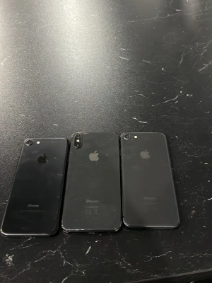 Svarta iPhones med glasbaksida - Tre svarta iPhones med stilren design och glasbaksida. Kan användas som reservdelar Två av modellerna har enkel kamera och en har dubbel kamera med vertikal placering. Alla har Apples logga på baksidan och rundade kanter. Perfekt för dig som gillar klassisk och modern mobilstil.