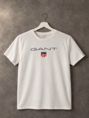 Vit t-shirt från GANT med tryck - Vit t-shirt från GANT med klassiskt tryck på bröstet och rund hals. T-shirten har korta ärmar och en normal passform. Perfekt till jeans eller shorts för en clean och enkel stil.