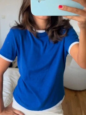 T-shirt  - En klassisk blå t-shirt med vita kanter vid ärmslut och halsringning. 